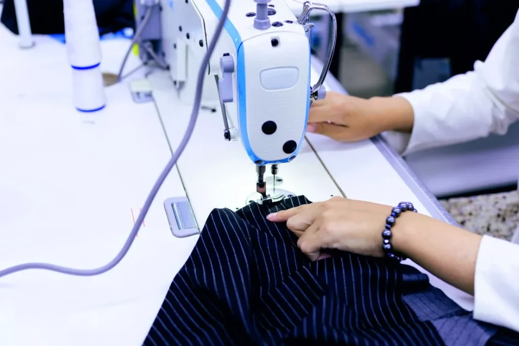Close-up of a tailor guiding striped navy fabric through an industrial sewing machine