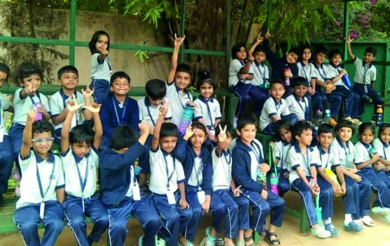 Primary school children in white shirts, navy trousers and ties, sitting outdoors and smiling